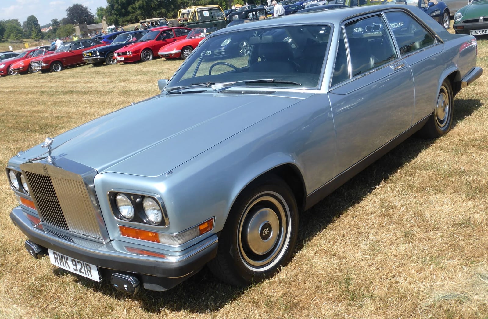 A light blue Rolls-Royce Camargue parked on dry grass at a show
