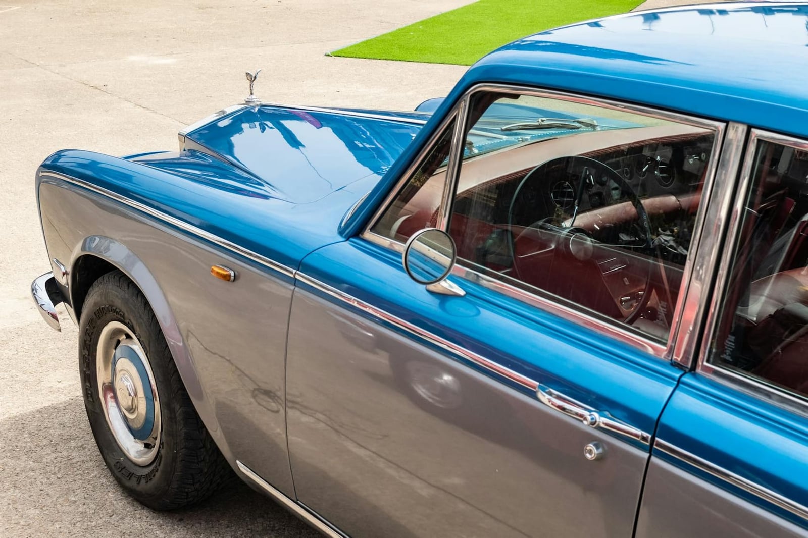 The flank and rear window of a bright blue Rolls-Royce Silver Shadow with red leather interior