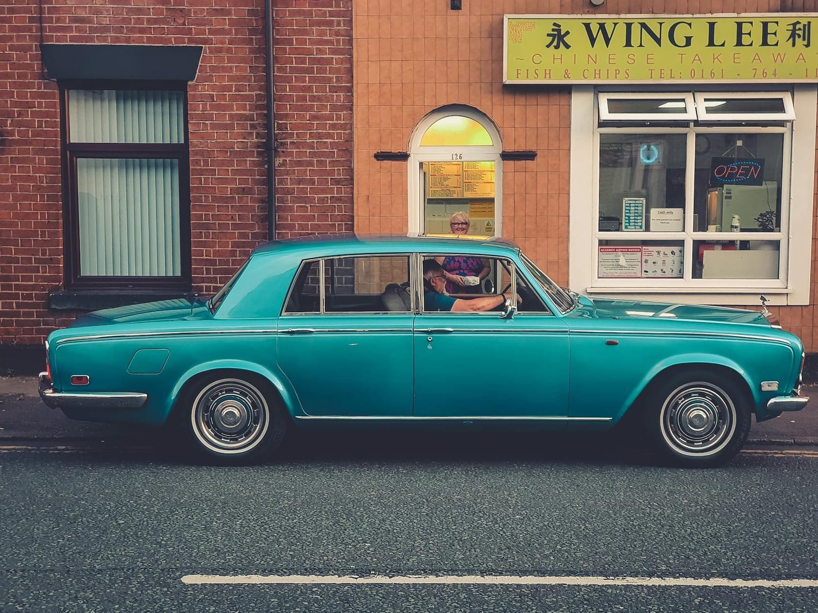 A teal Rolls-Royce Silver Shadow parked outside a Chinese takeaway on a British street