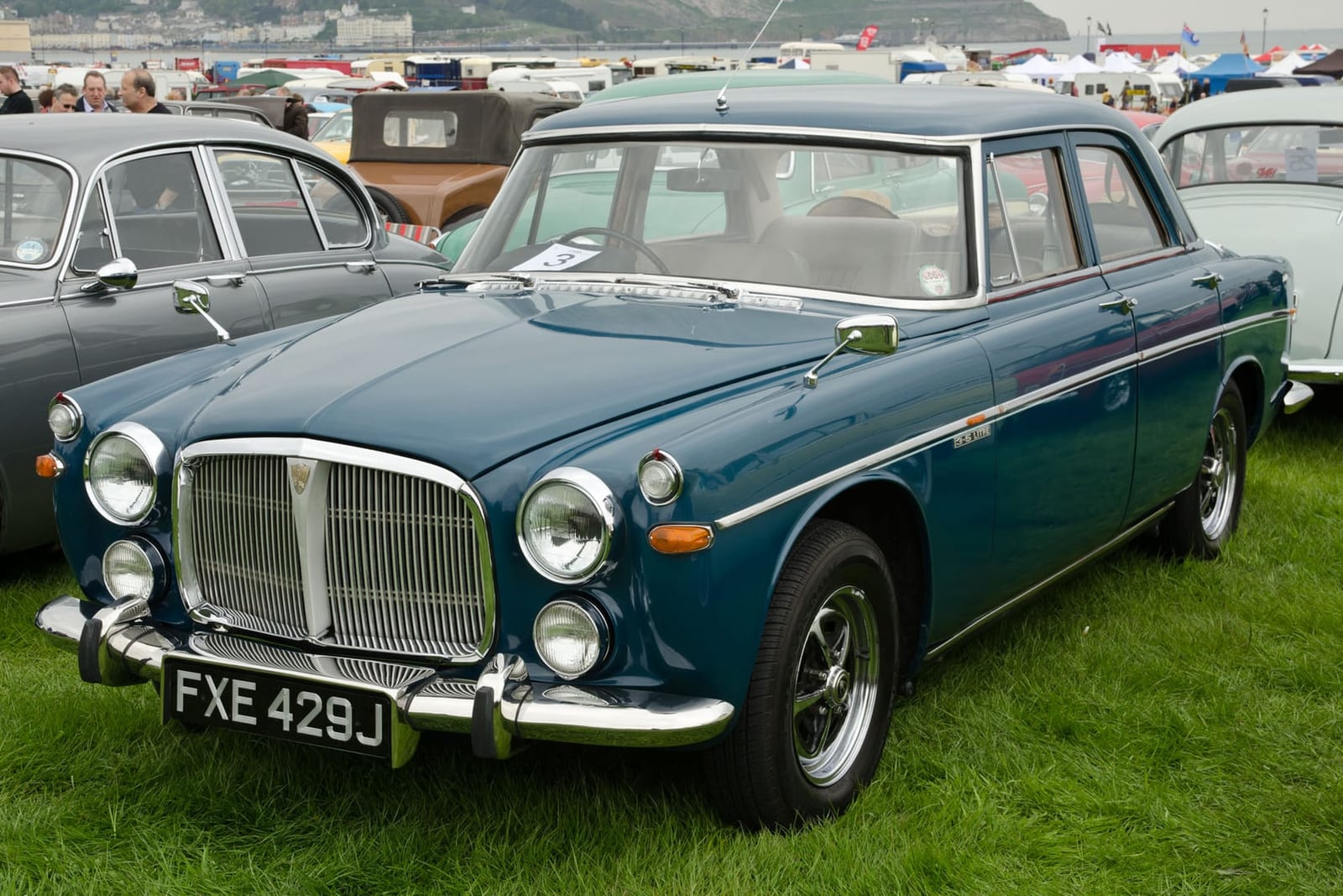 A teal 1971 Rover P5B coupe on grass at a classic car show, front three-quarter view, UK registration FXE 429J