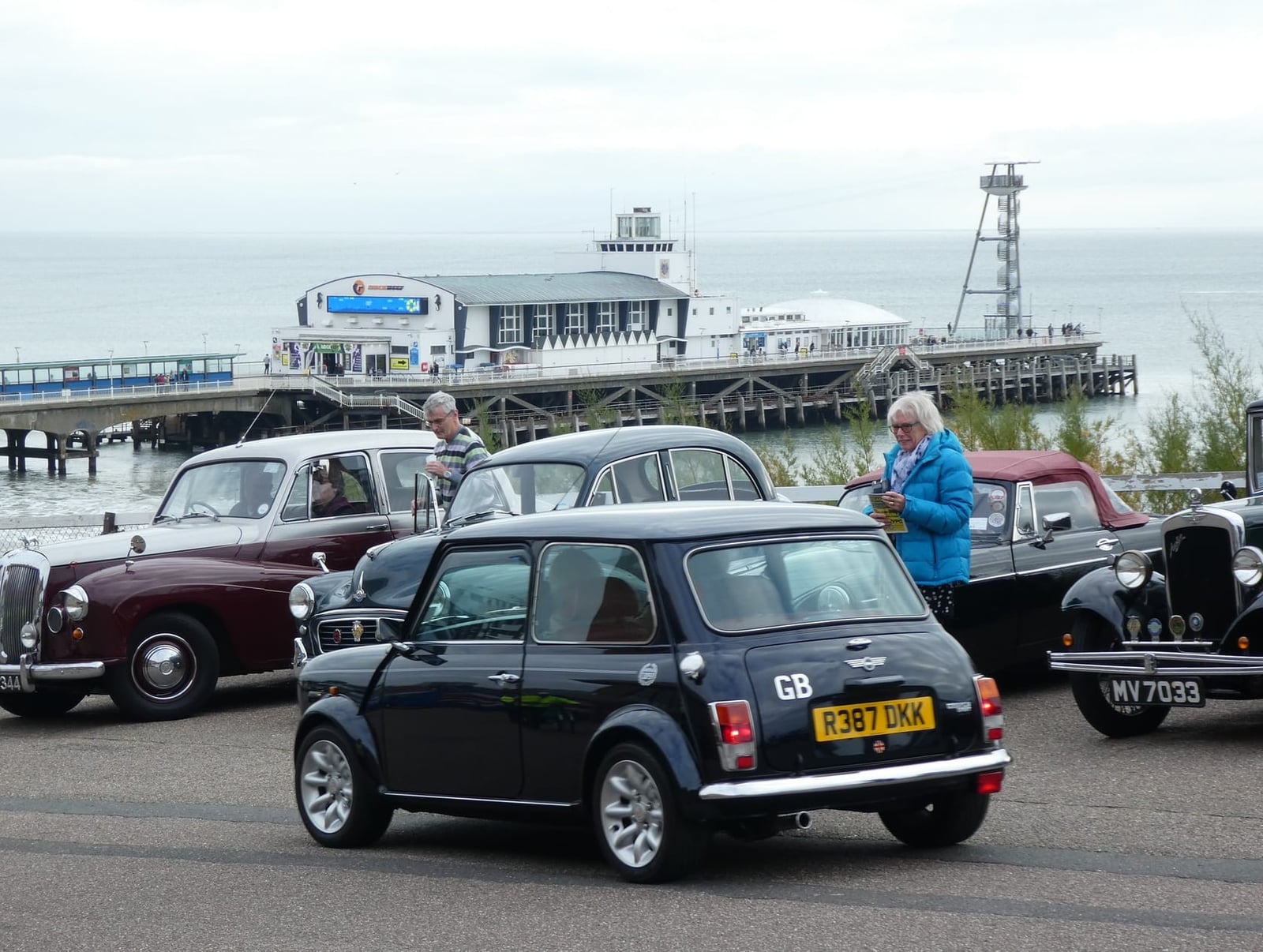 A dark 1998 Rover Mini Cooper with a UK registration parked on a seafront, a pier behind