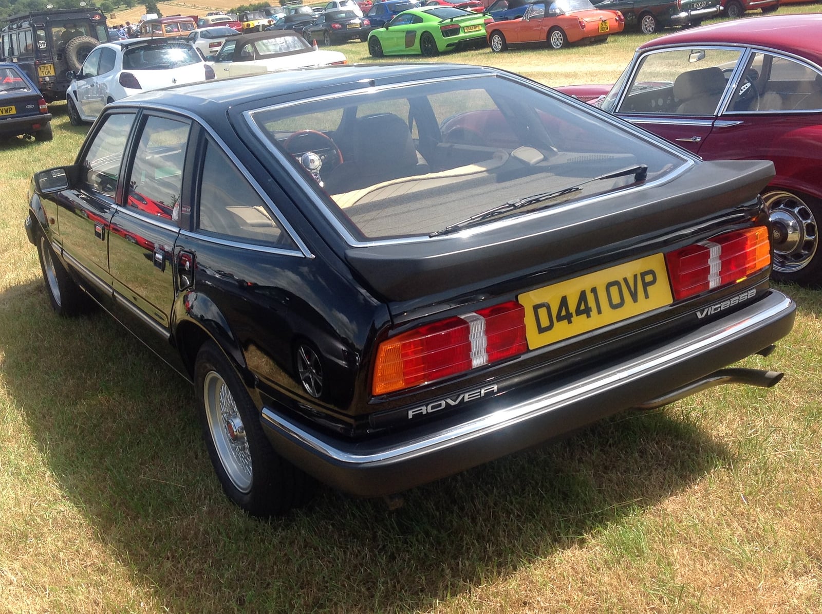 A black Rover SD1 Vitesse, rear three-quarter view, its sloping fastback roofline running down to a lifting tailgate, on grass at a show