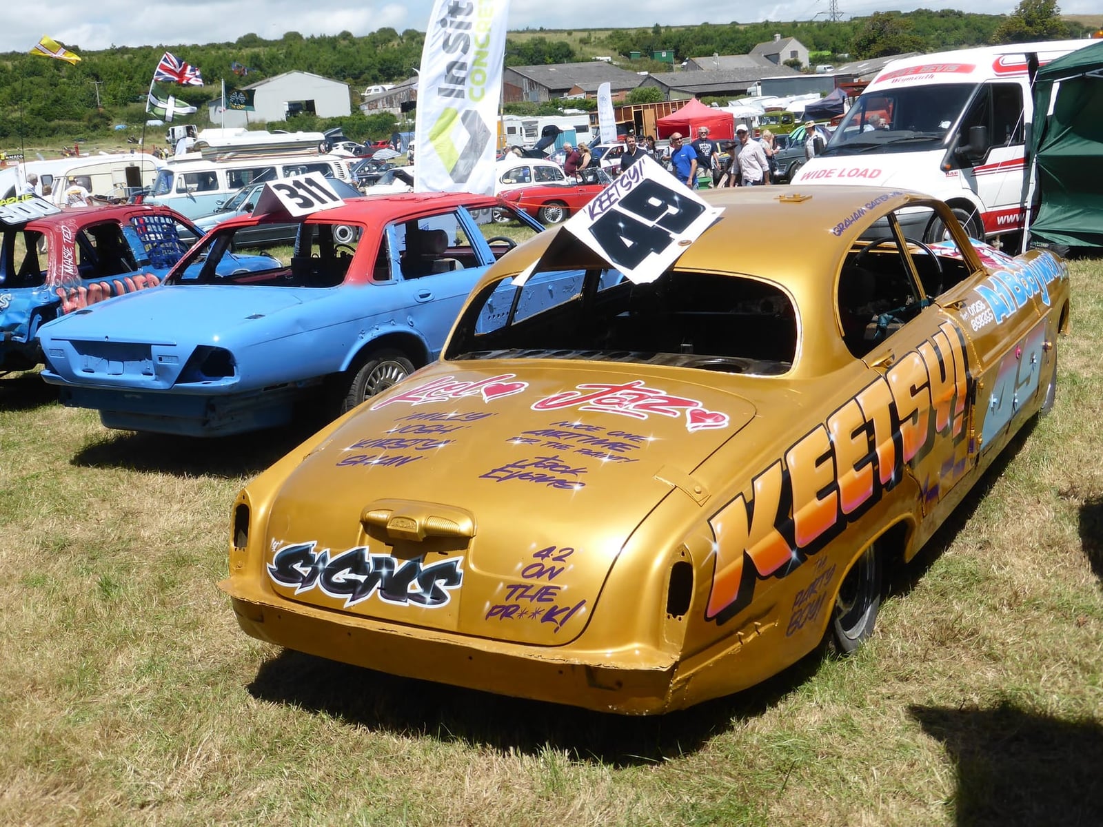 A blue Jaguar Mk X saloon parked among vans at a show, rear three-quarter view, UK registration 180 MDV