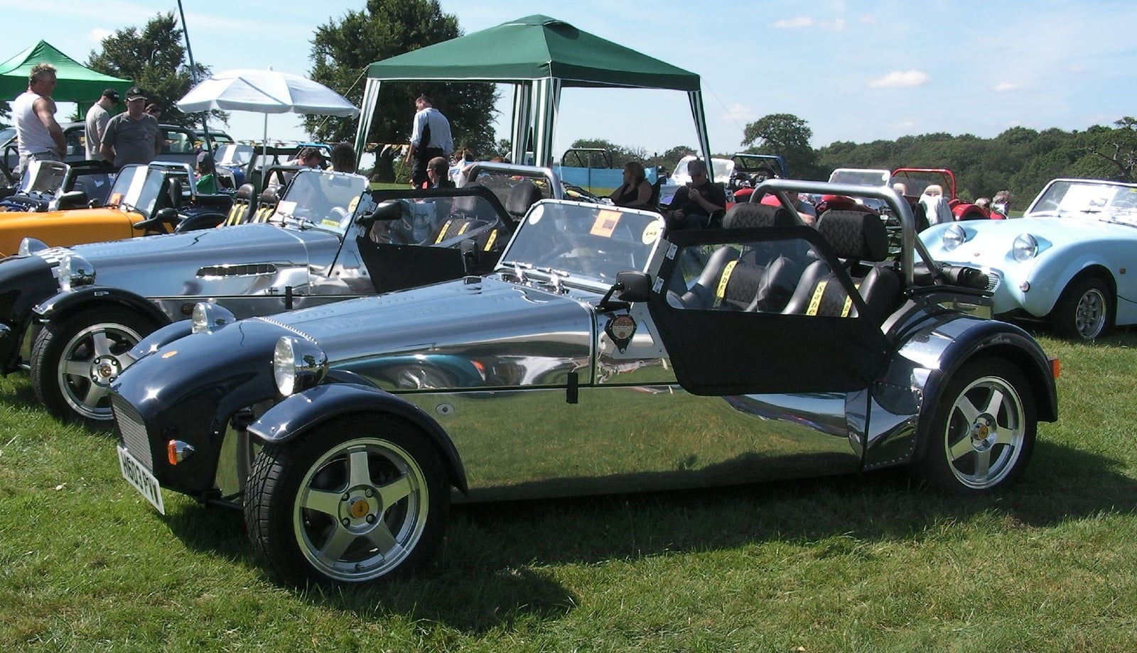 A Robin Hood Seven-style roadster with a bare polished stainless-steel body and black wings, at a classic car show
