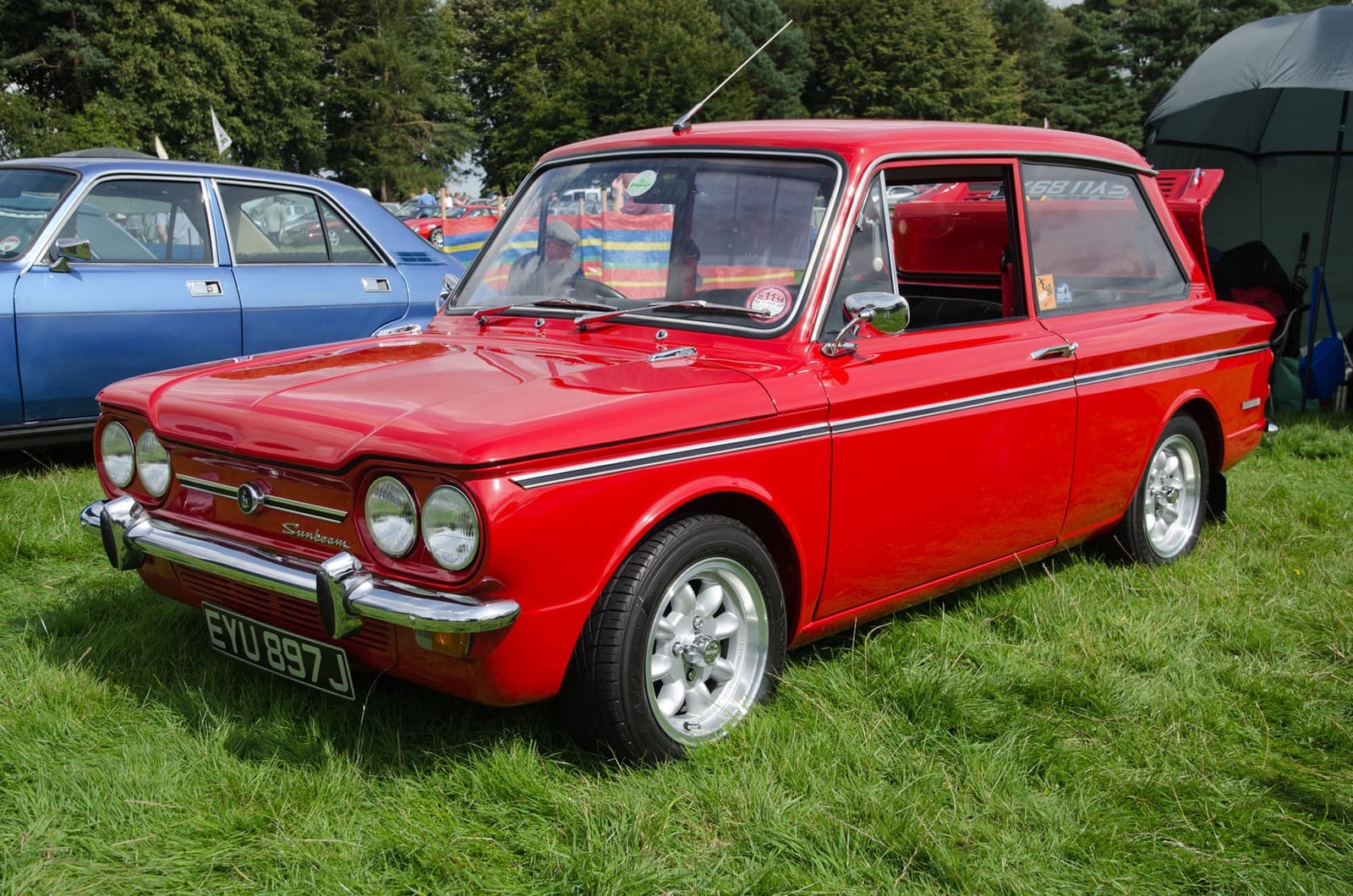 A red Sunbeam Imp Sport with alloy wheels, front three-quarter view on grass