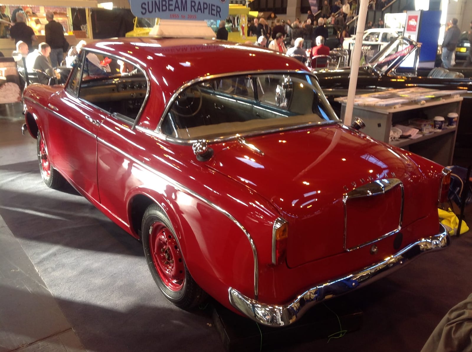 The rear three-quarter of a red and black 1955–56 Sunbeam Rapier Series I at an indoor show