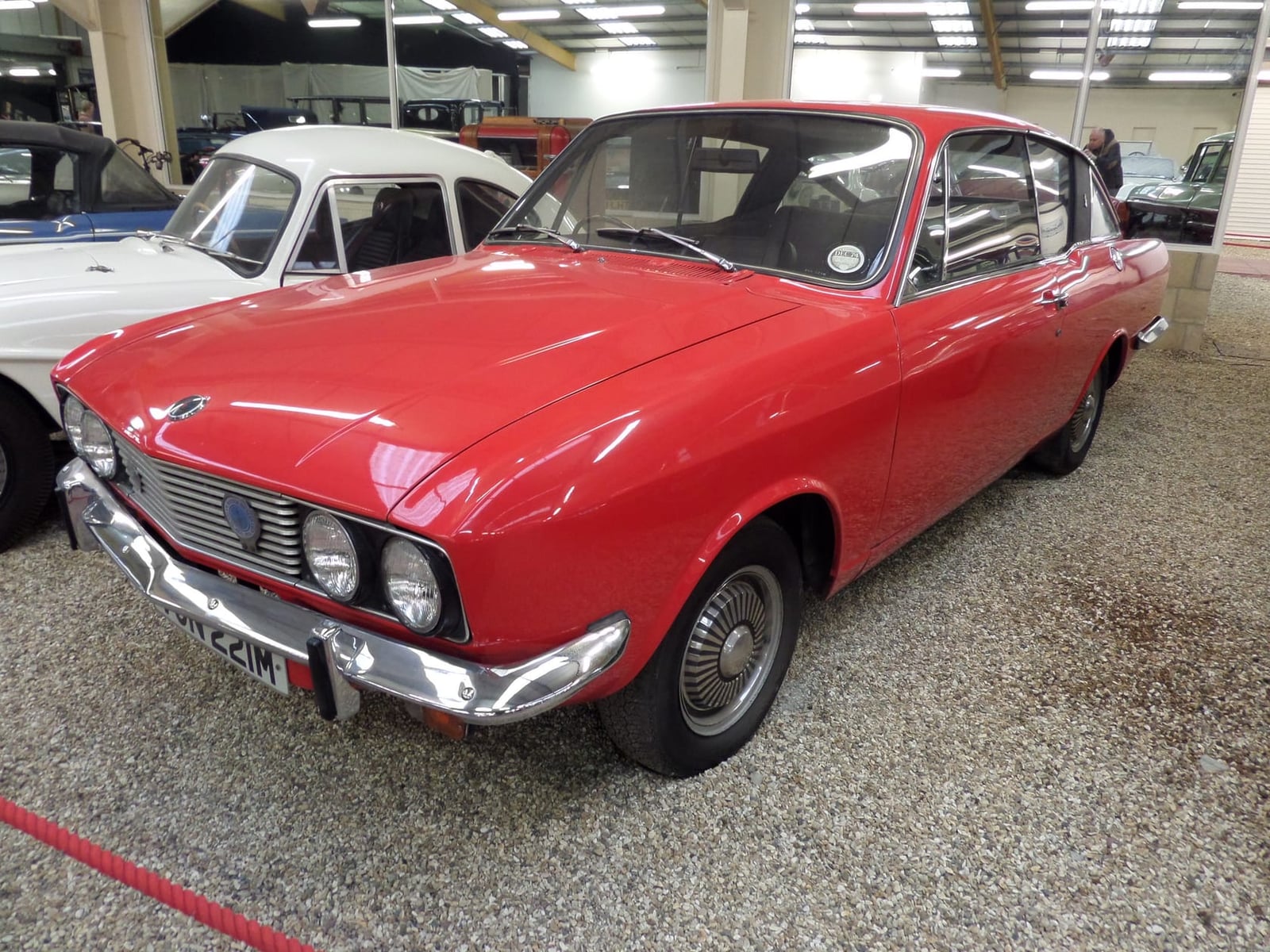 A red Sunbeam Rapier fastback from the mid-1970s parked indoors, front three-quarter view