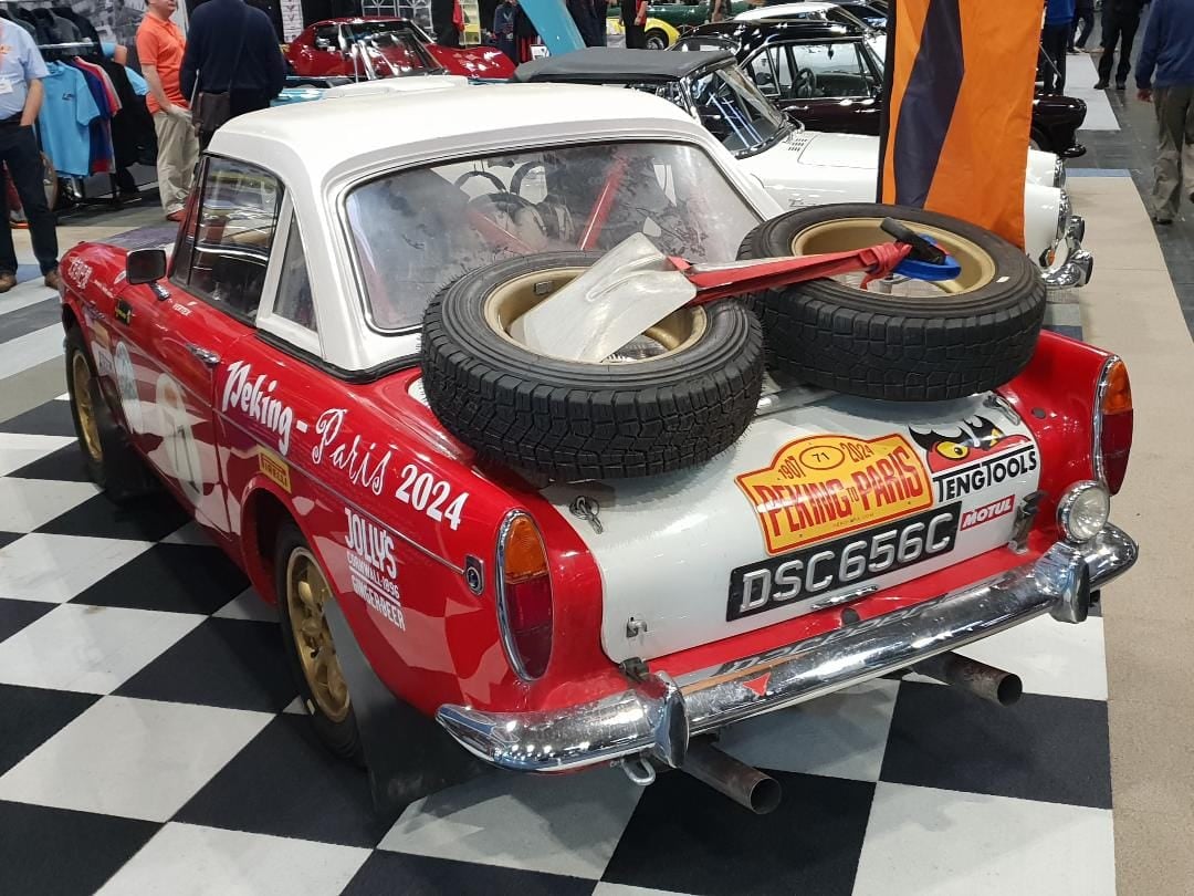 A red and white 1965 Sunbeam Tiger in endurance rally trim with spare wheels strapped to its boot