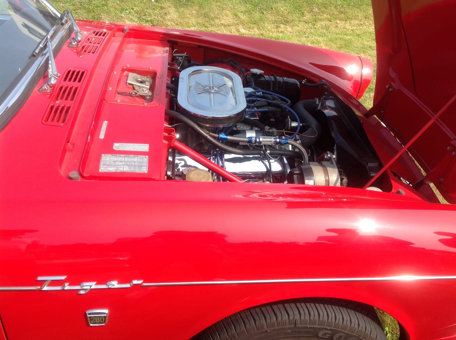 The engine bay of a red Sunbeam Tiger showing the Ford V8 and Tiger script