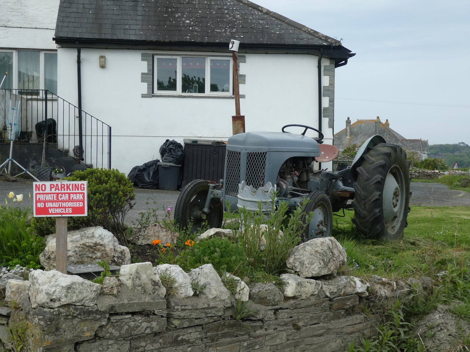 A grey Ferguson TE20 parked by a whitewashed Cornish cottage and dry-stone wall, the sea beyond