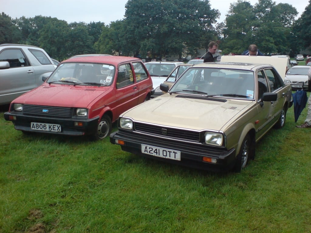 A red and a beige Triumph Acclaim parked side by side on grass at a classic car show