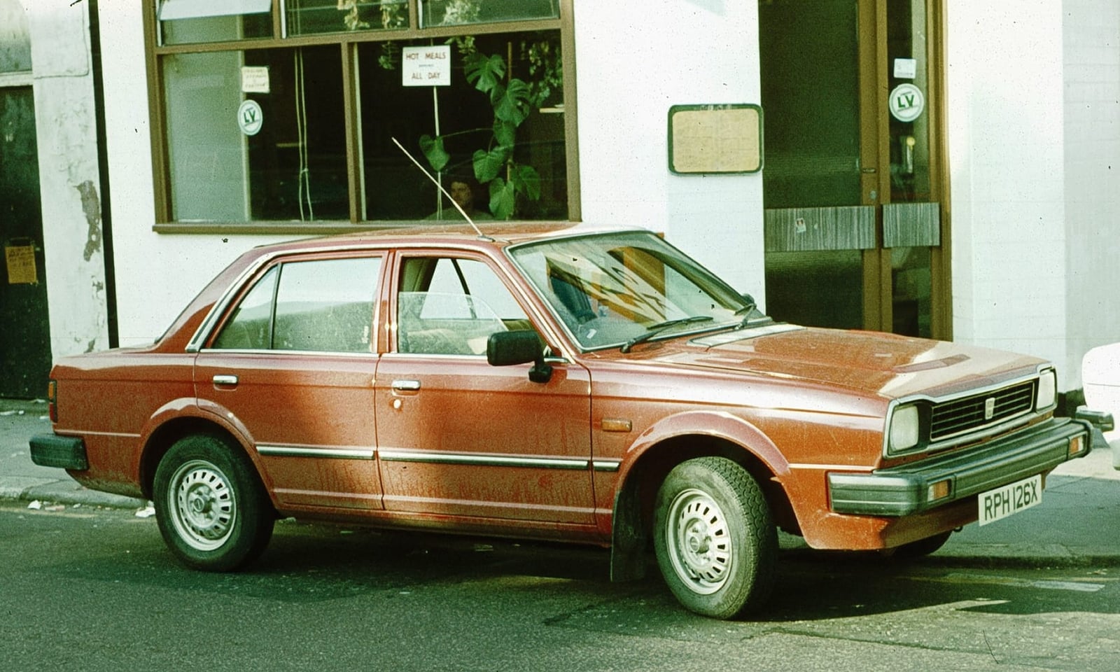A brown Triumph Acclaim parked outside a building in period, side view