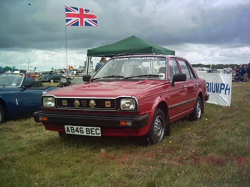 A red Triumph Acclaim on a club stand at a classic car rally with a Union flag flying behind, UK registration A846 BEC