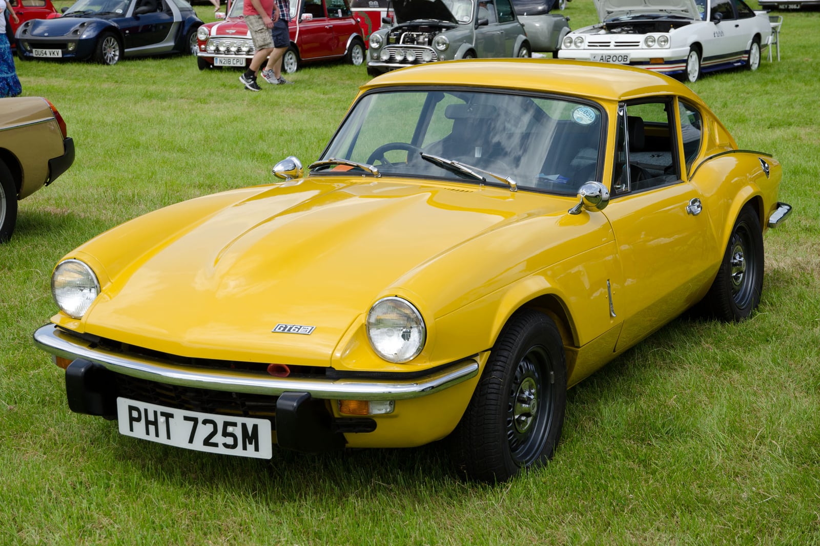 A yellow Triumph GT6 Mk3 fastback coupe, front three-quarter view on grass