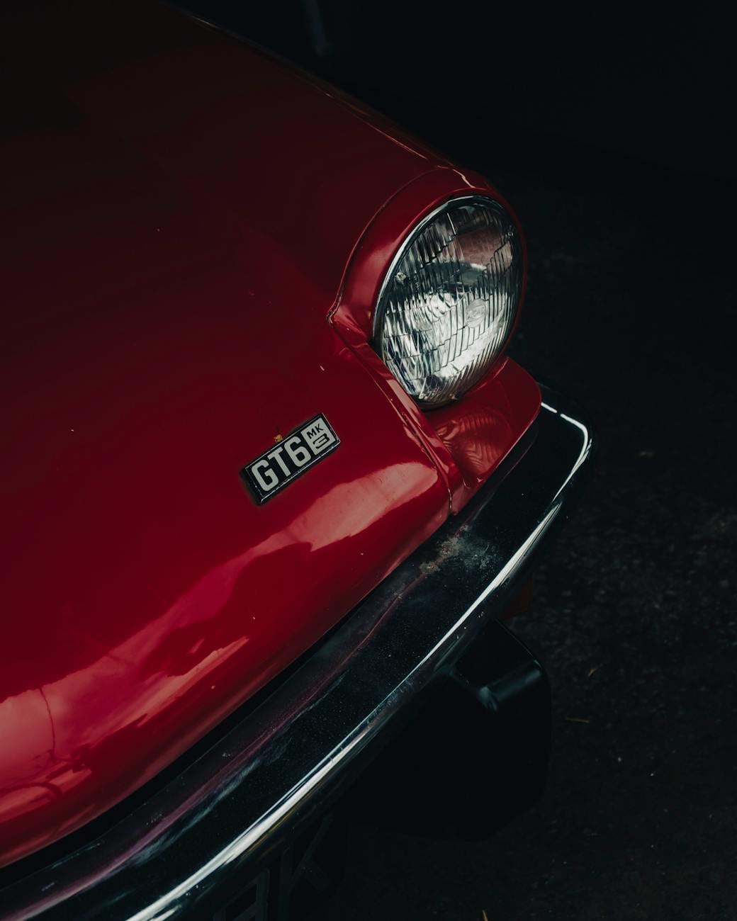 Close-up of the GT6 Mk3 badge and headlamp on the nose of a red Triumph GT6