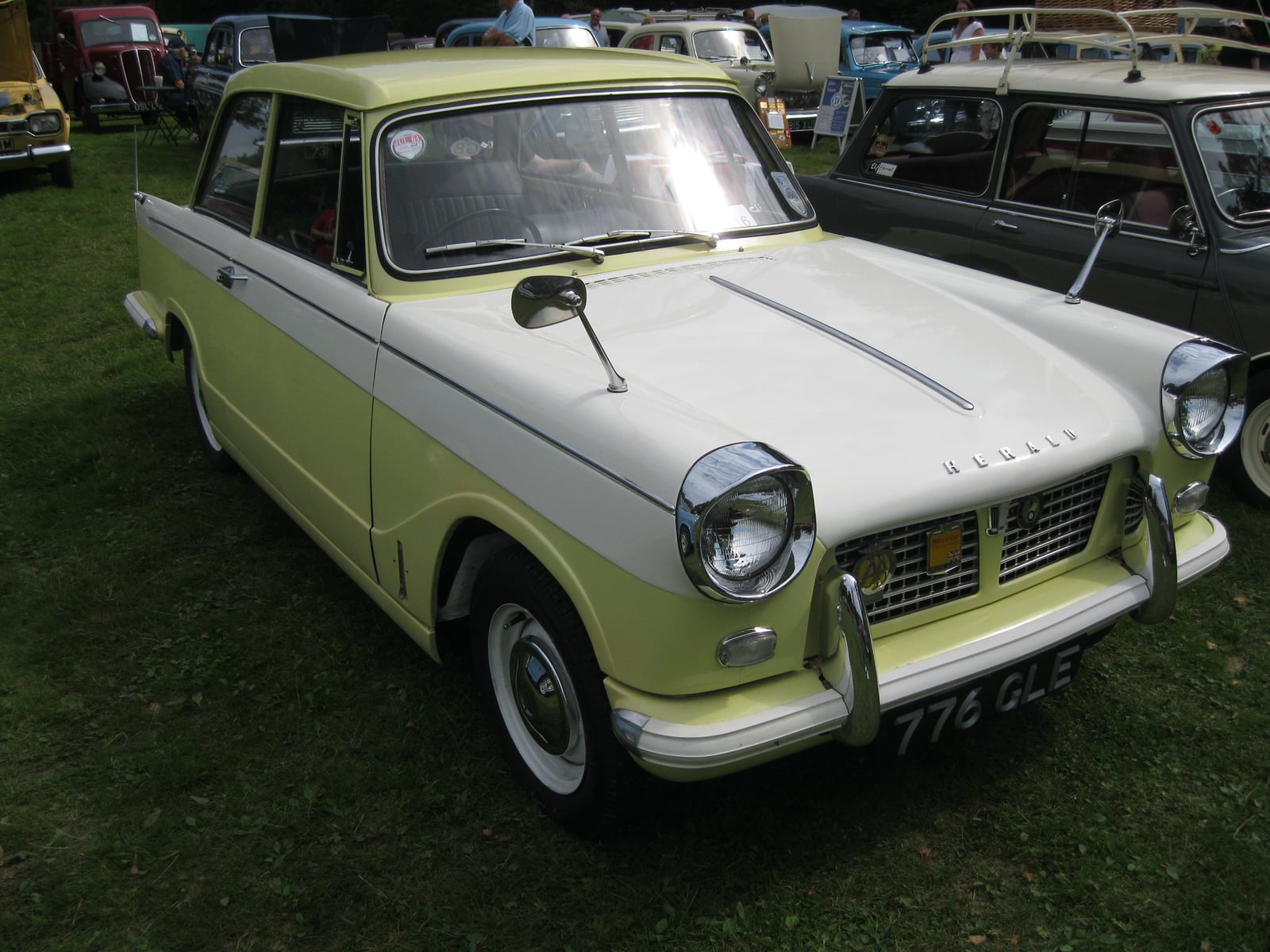 A yellow and white two-tone Triumph Herald 1200 saloon, front three-quarter view on grass