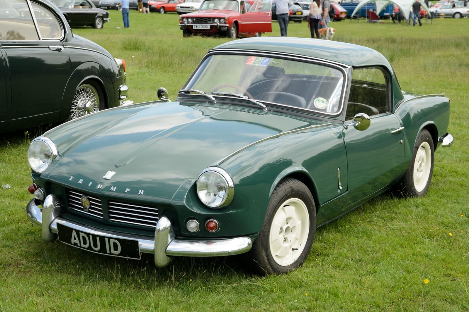 A dark green 1967 Triumph Spitfire Mk2 with its factory hardtop and a UK registration on a show field