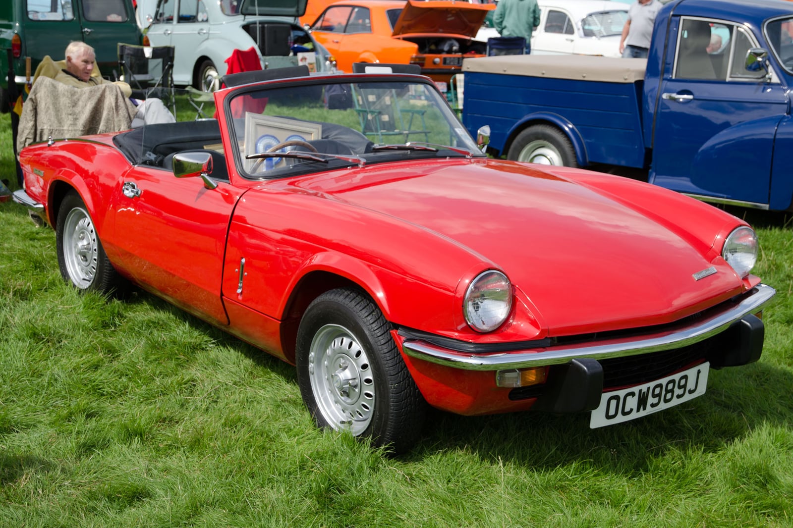 A red Triumph Spitfire Mk4, top down, front three-quarter view on grass at a show