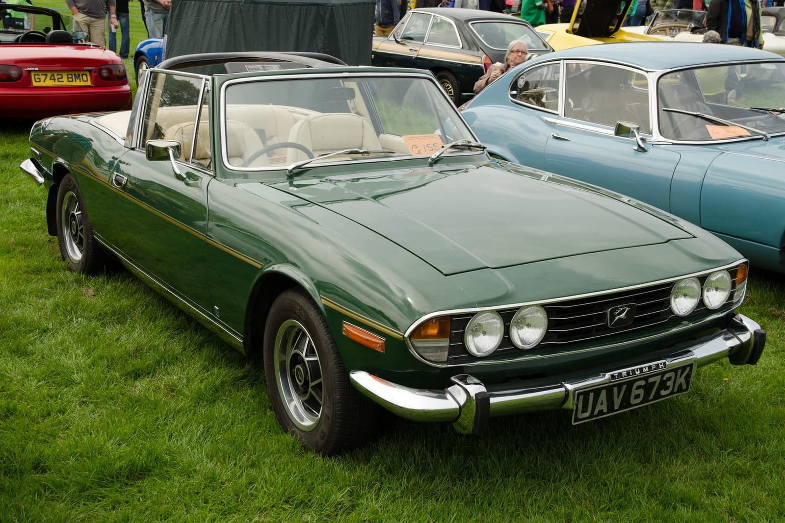 A dark green 1971 Triumph Stag Mk1 with its T-bar and hood up and a UK registration on a show field