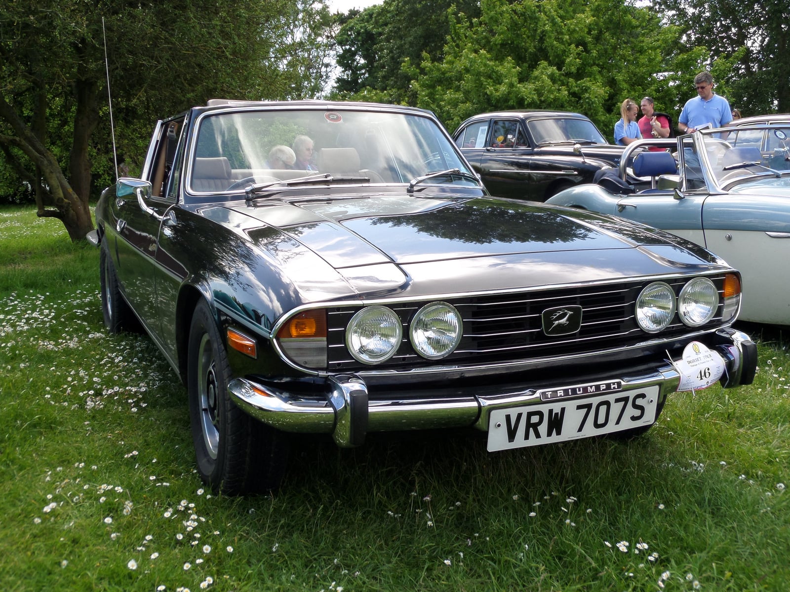 A dark Triumph Stag with the top down, showing the T-bar, front three-quarter view on grass