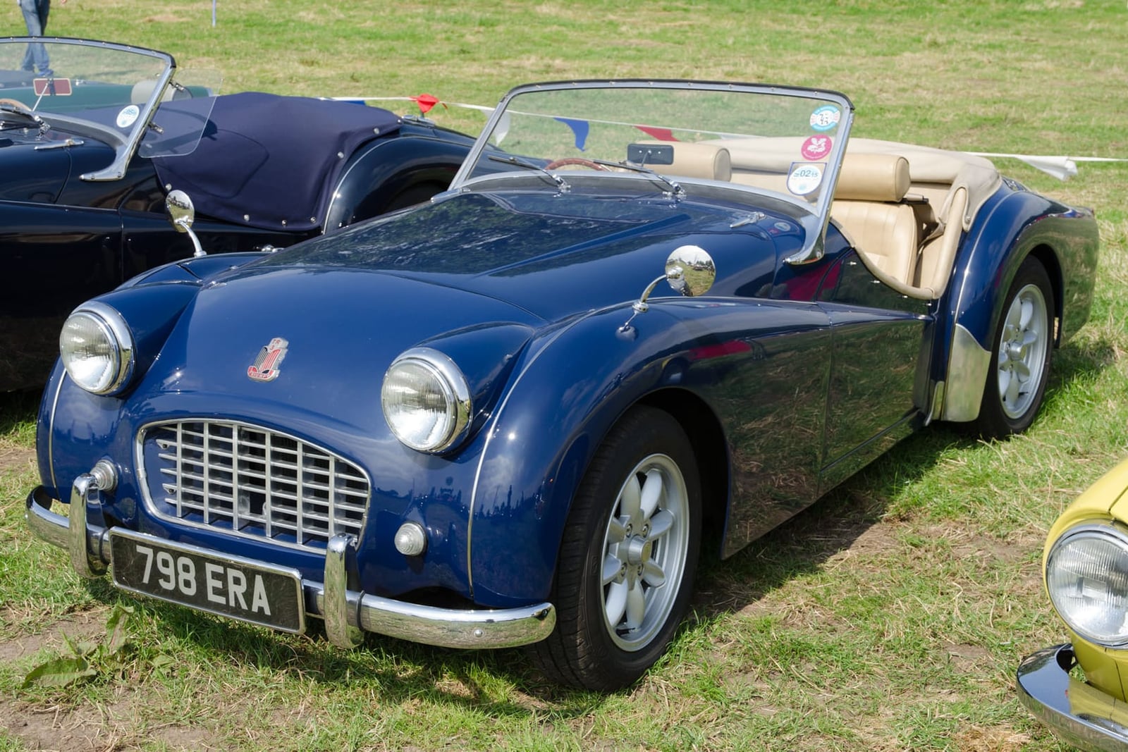 A dark blue 1957 Triumph TR3A with a UK registration and its hood down on a show field