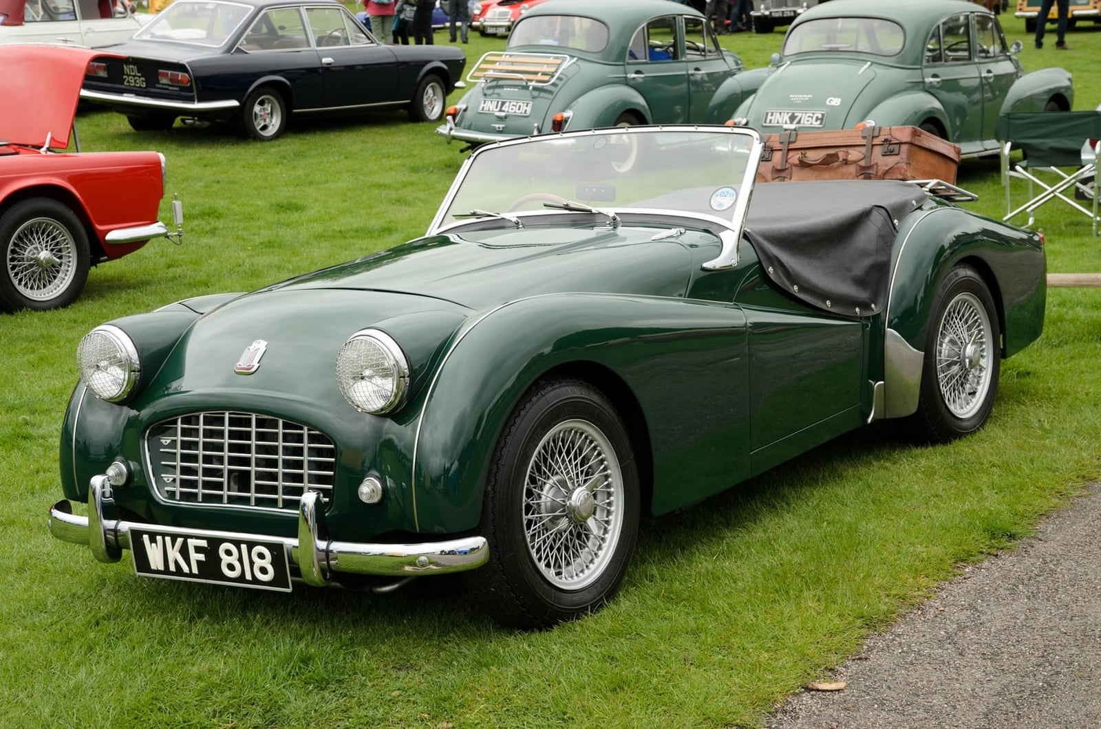 A dark green 1957 Triumph TR3 with a suitcase on its rear luggage rack and a UK registration at a show