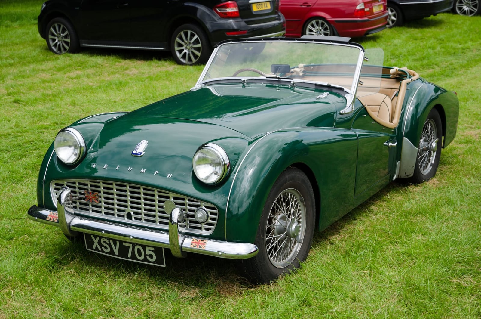 A dark green 1959 Triumph TR3A with wire wheels and a UK registration on grass at a show