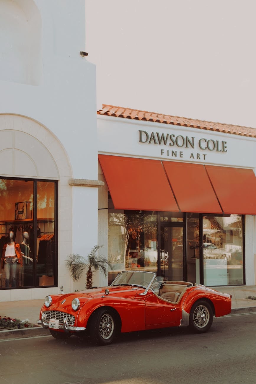 A red Triumph TR3 roadster with the hood down, parked at a kerb