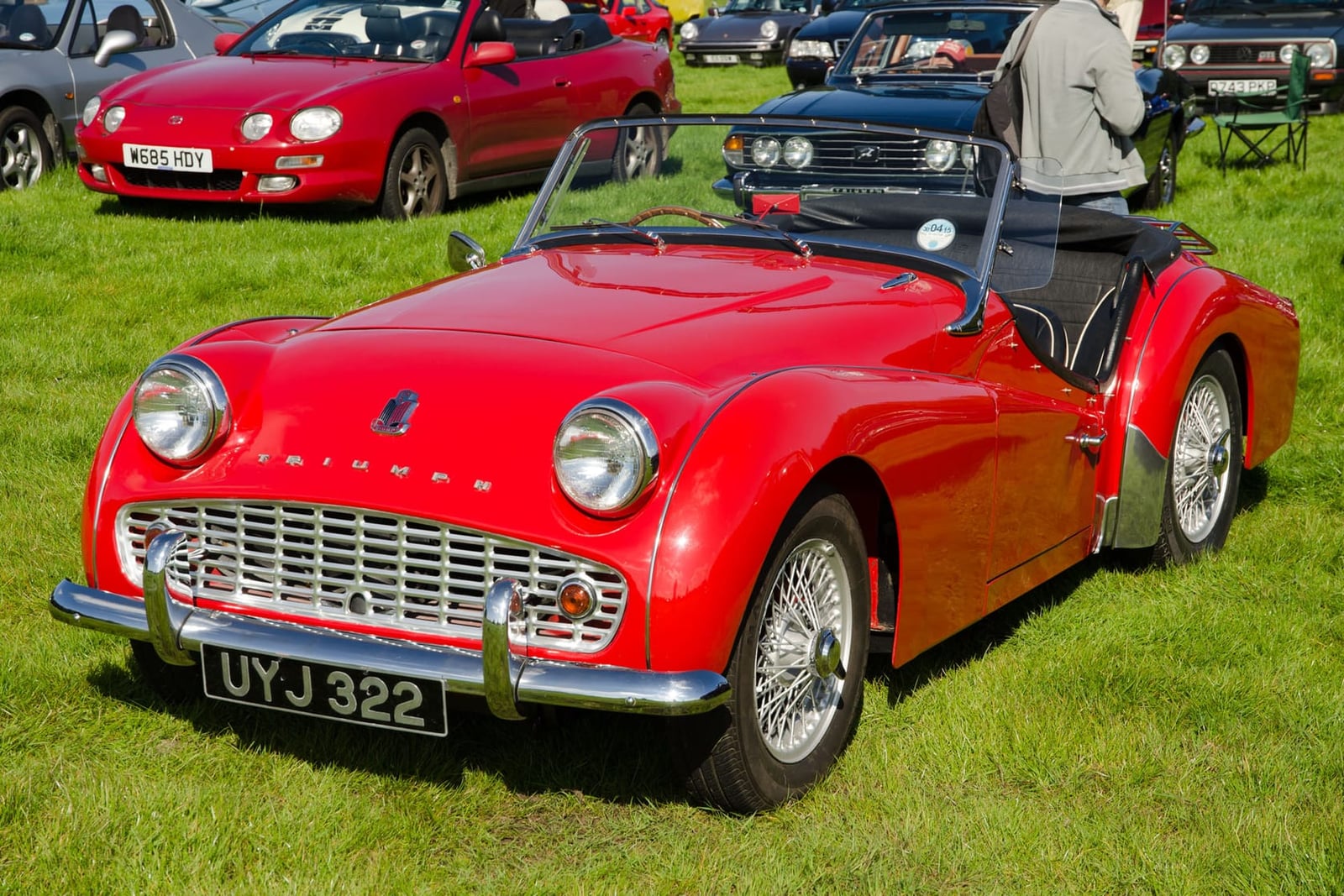 A red 1962 Triumph TR3B 2.2 with wire wheels and a UK registration on a show field