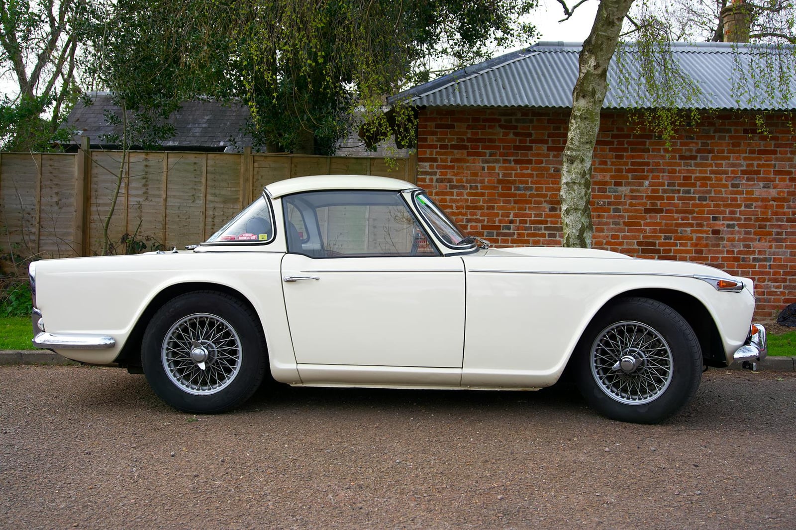 A white Triumph TR4 with its Surrey-top hardtop fitted, clean side profile