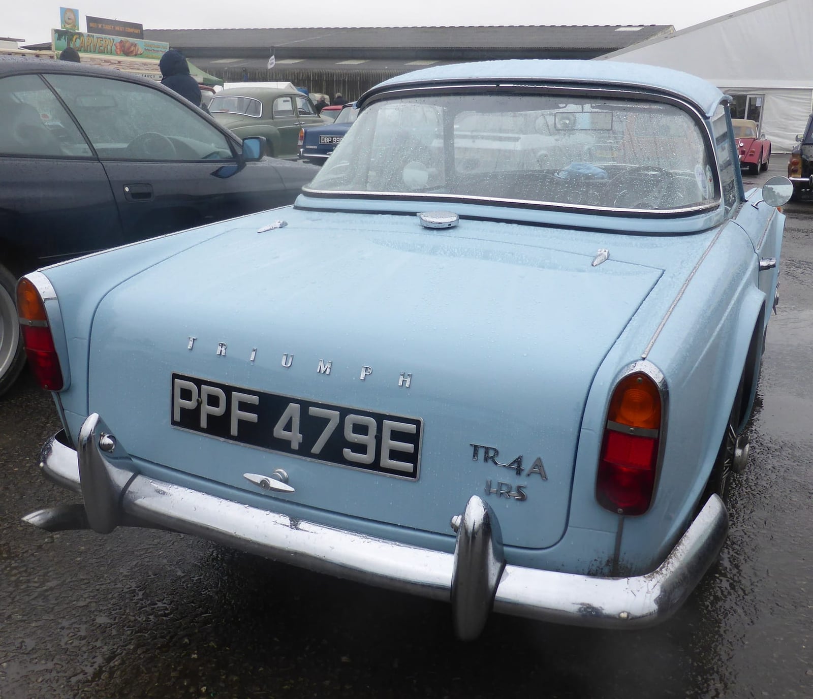 The rear of a pale blue 1967 Triumph TR4A with its IRS badge and a UK registration in a wet car park