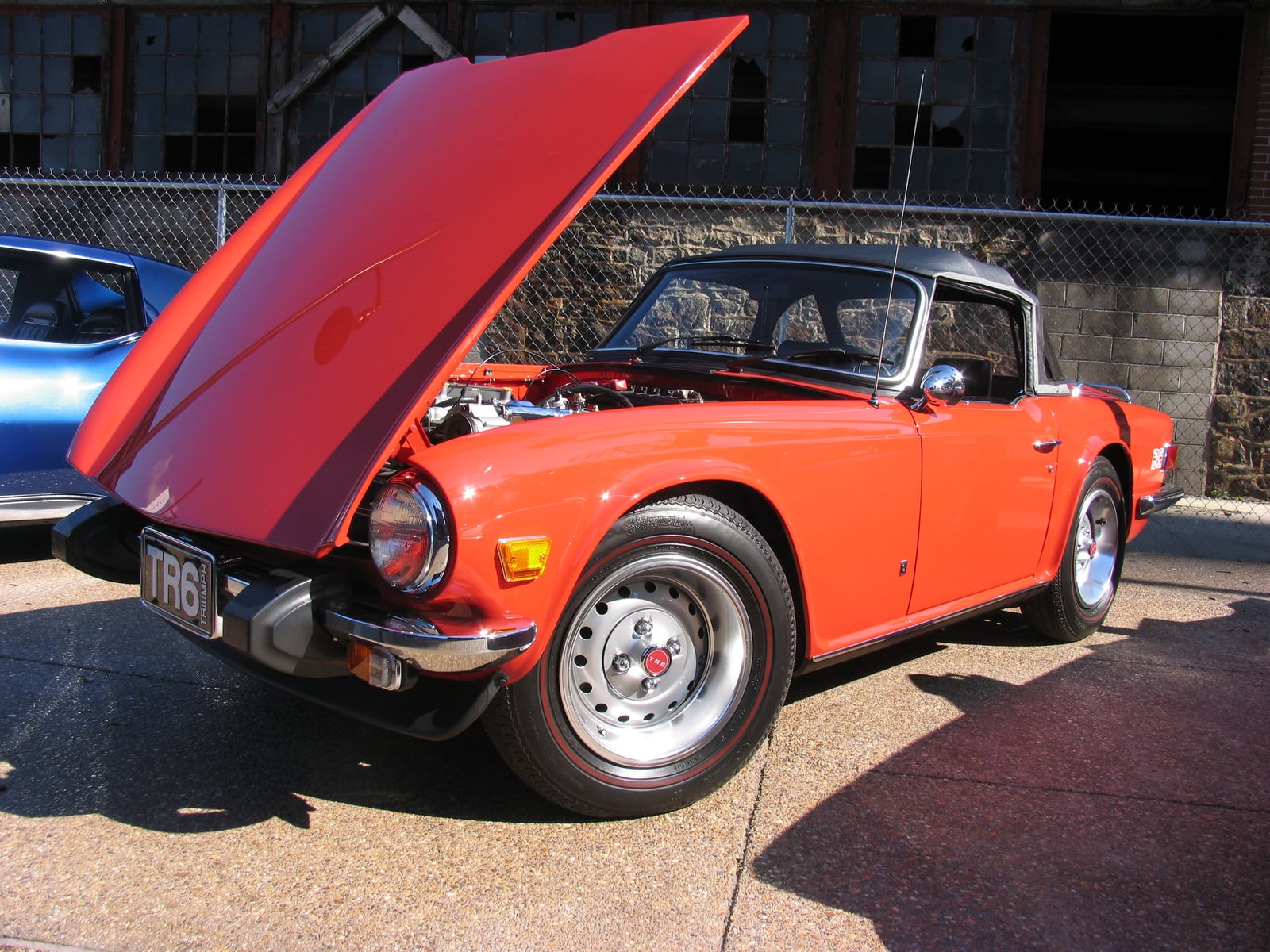 An orange Triumph TR6 with the bonnet raised, showing the straight-six engine, at a show