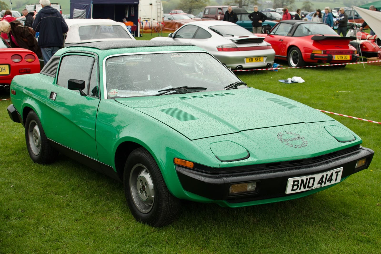 A green 1978 Triumph TR7 fixed-head coupe at a classic car show, front three-quarter view, UK registration BND 414T