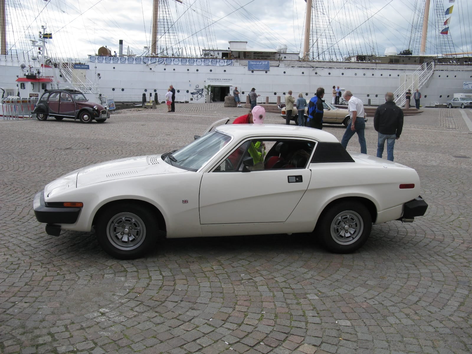 A white Triumph TR7 coupe in side profile on a harbour quay