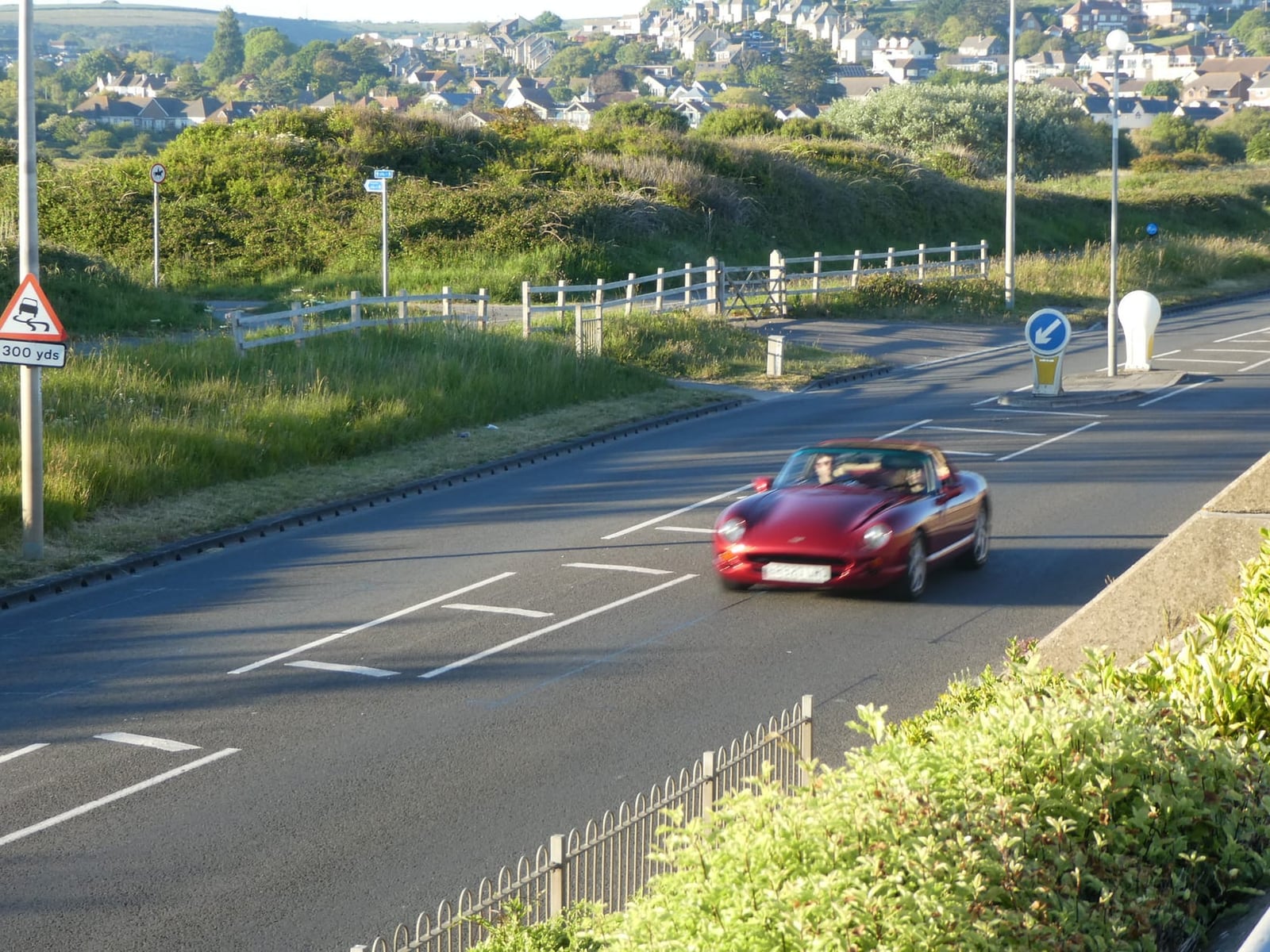 A red TVR Chimaera being driven on a country road with the hood down