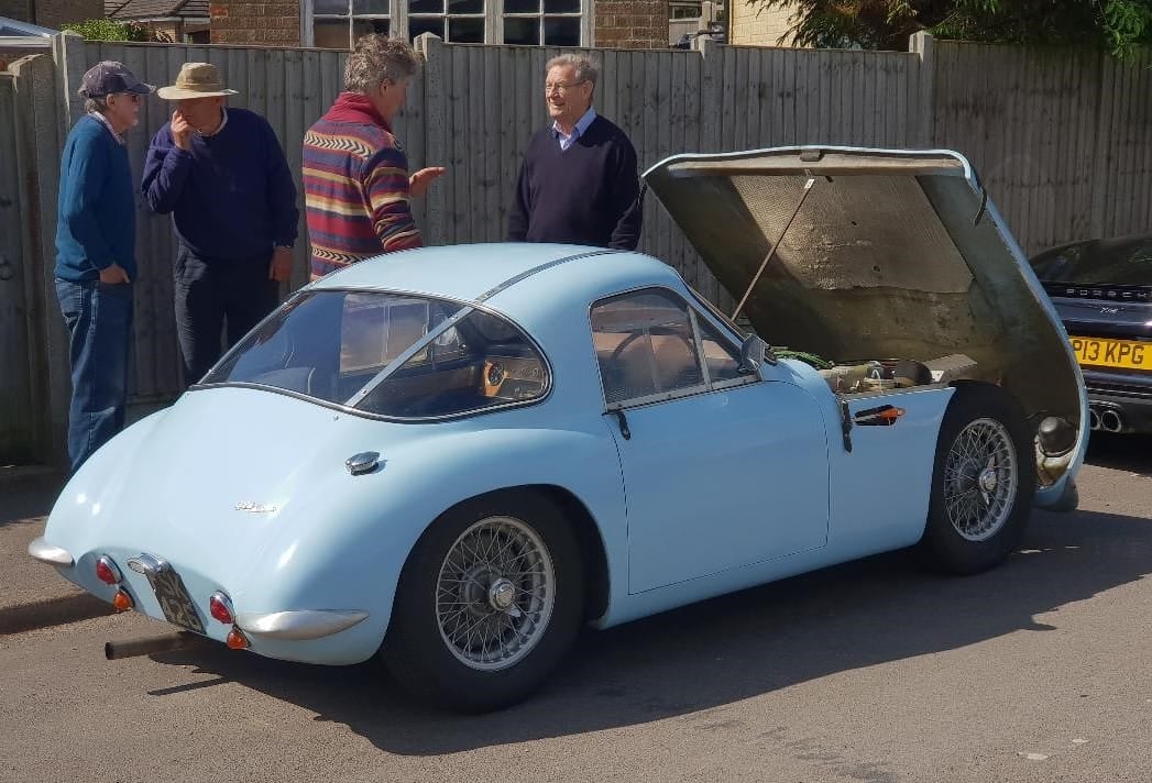 A light blue 1959 TVR Grantura with its bonnet open at a classic car gathering