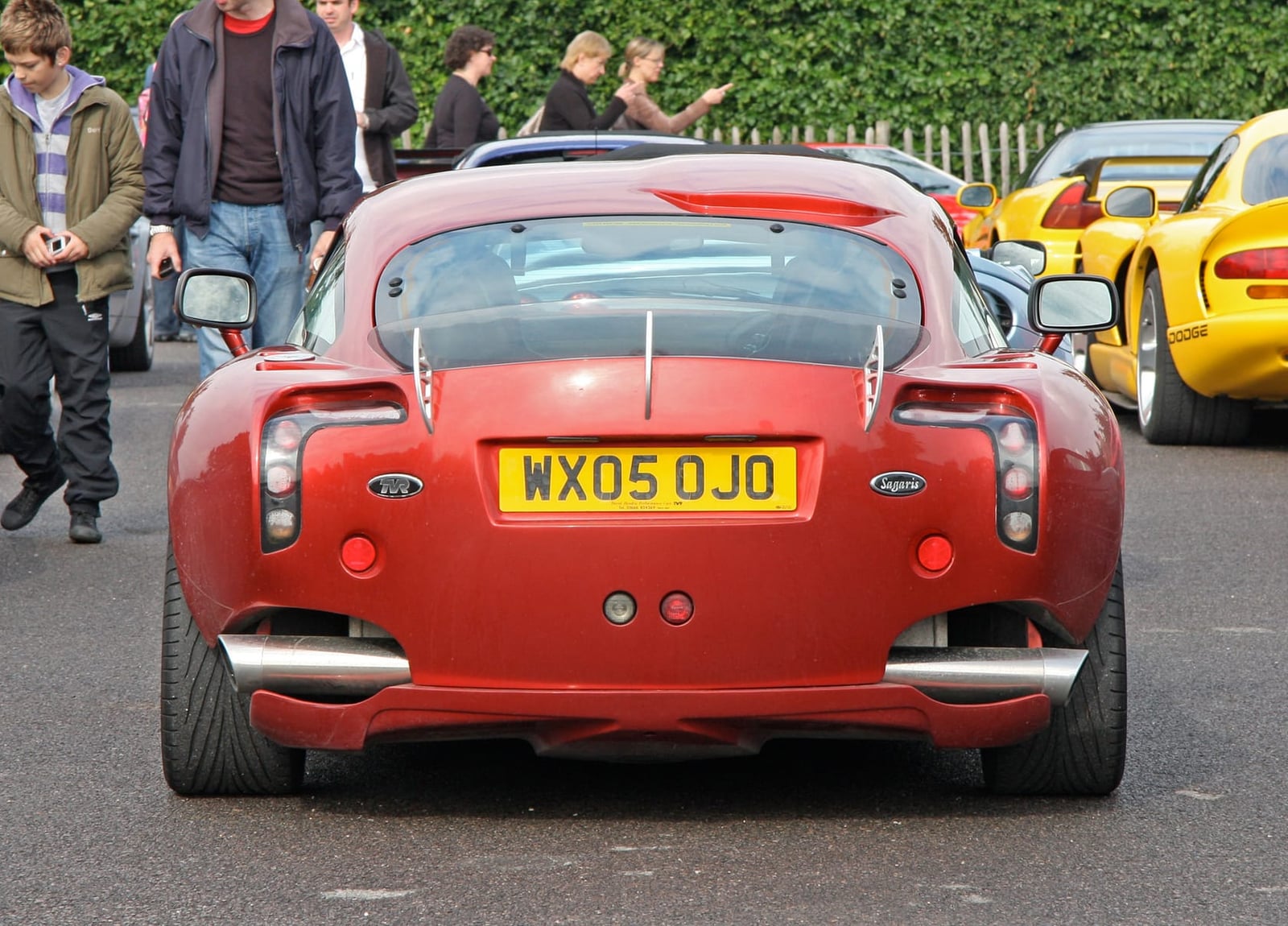 The rear of a red 2005 TVR Sagaris with a UK registration at a show, its transparent spoiler and side-exit exhausts visible