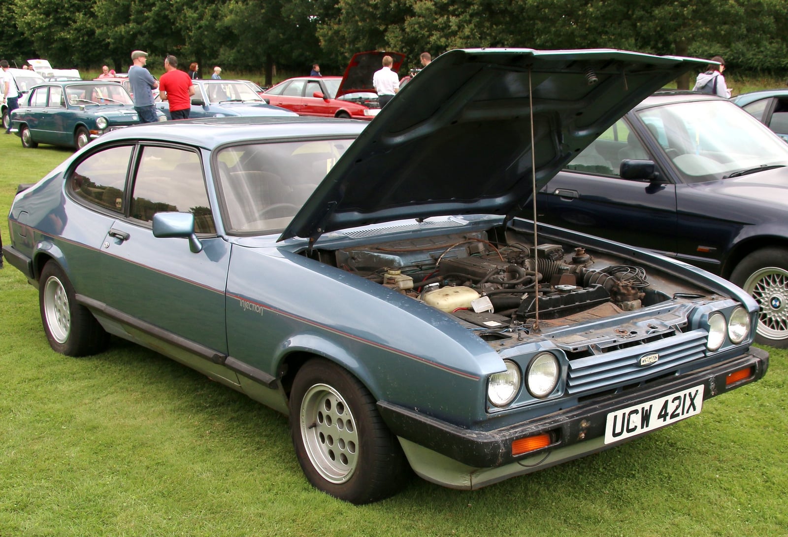 A metallic blue Ford Capri 2.8 Injection with the bonnet raised, showing the V6 engine, at a show