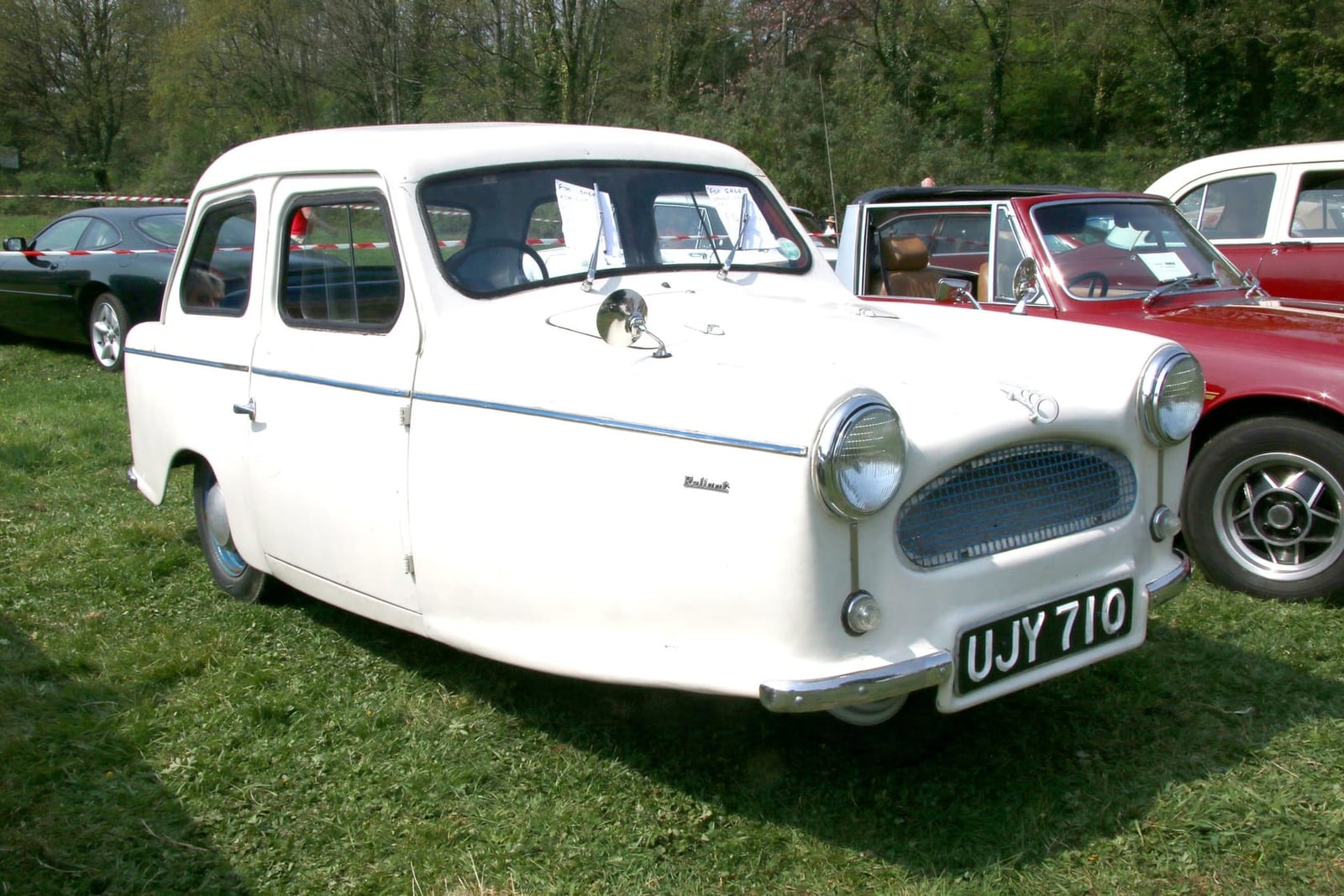A white 1961 Reliant Regal Mk6 on grass at a classic vehicle show, side view, UK registration UJY 710