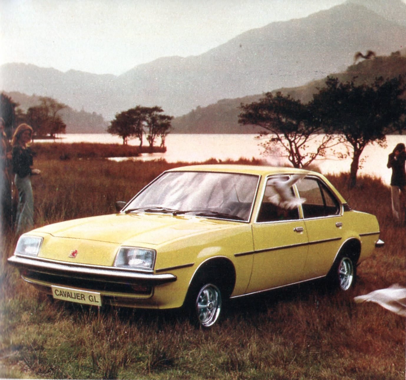 A period press photograph of a yellow 1976 Vauxhall Cavalier GL by a loch