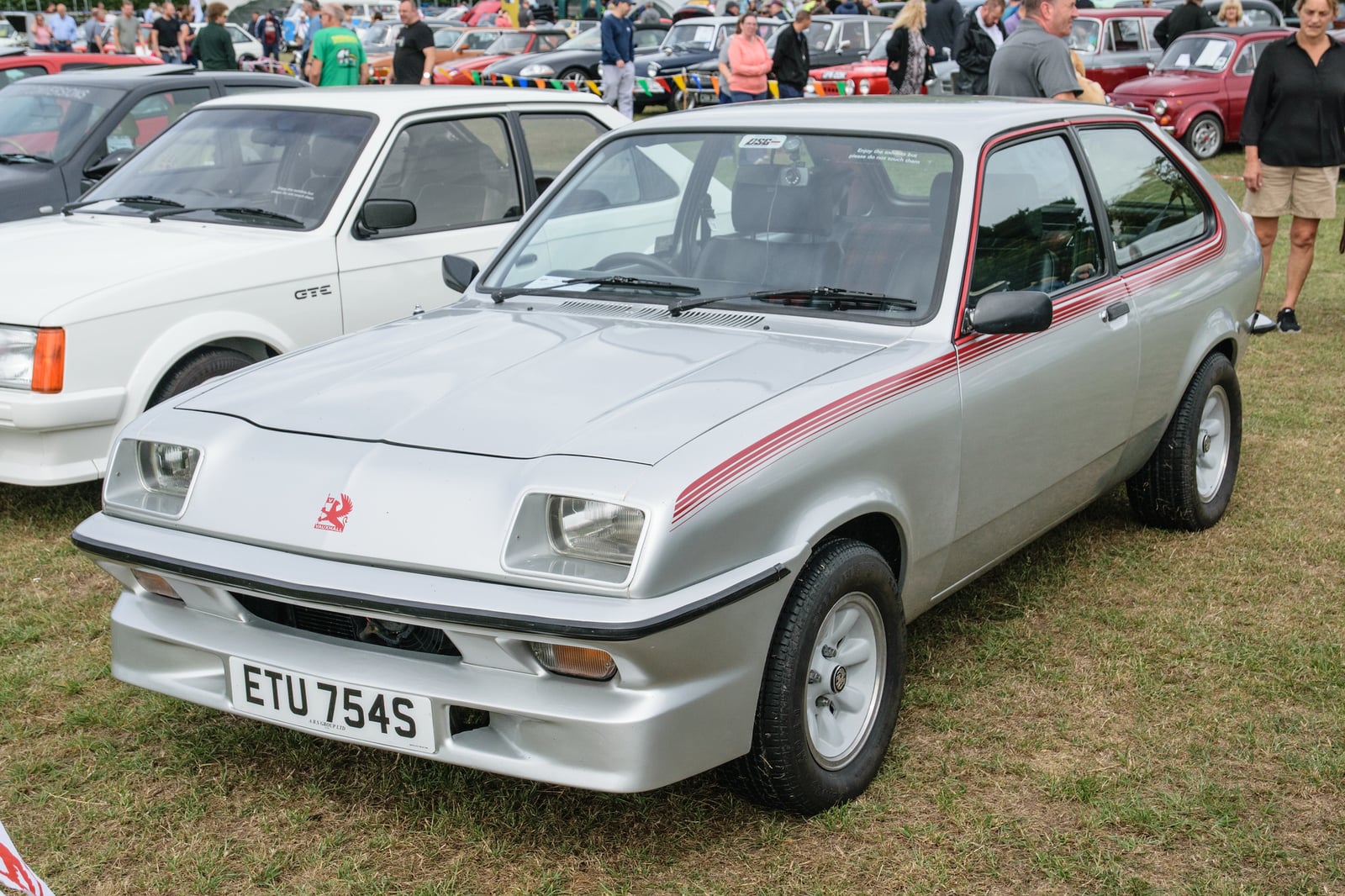 A silver Vauxhall Chevette HS (1978) with red side stripes, front three-quarter view at an outdoor classic car show