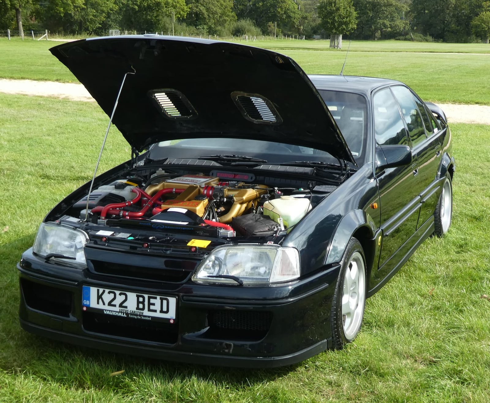 A dark green Lotus Carlton with its bonnet raised on a showfield, UK registration K22 BED
