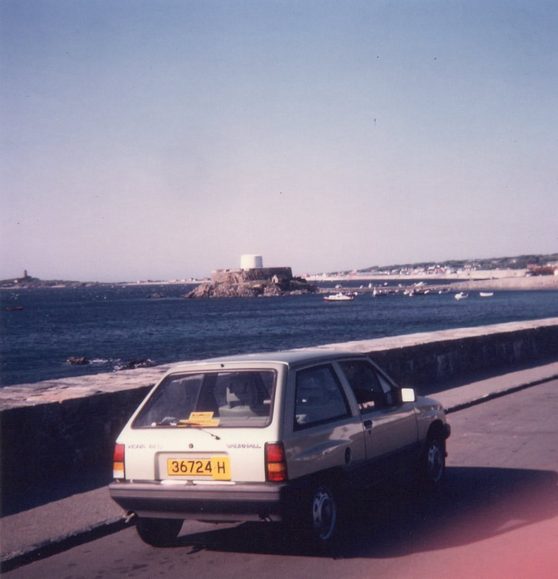 A period photograph of a white Vauxhall Nova parked by a seafront