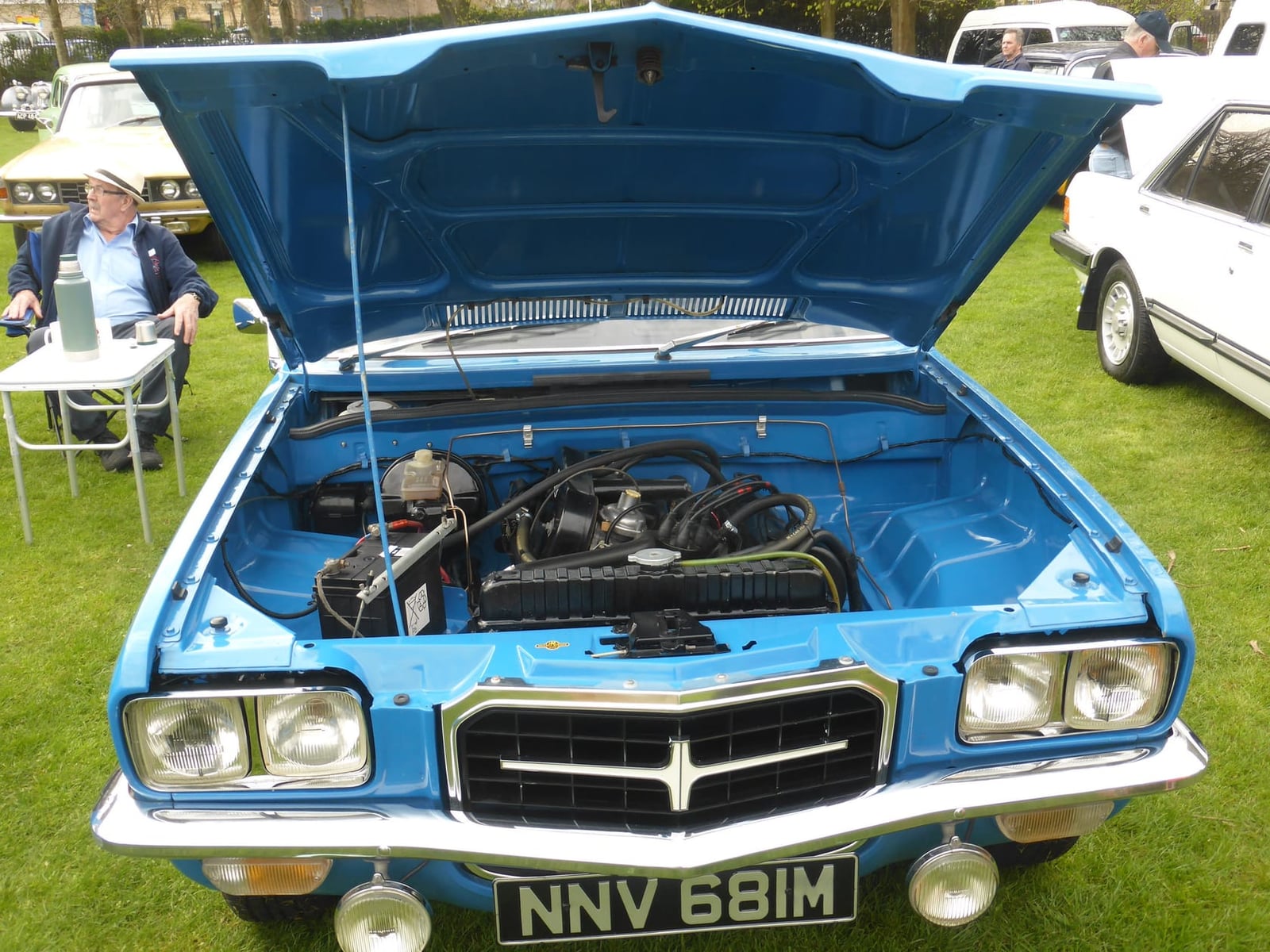 A blue Vauxhall VX4/90 FE with its bonnet raised at a classic car show, showing the slant-four engine, UK registration NNV 681M