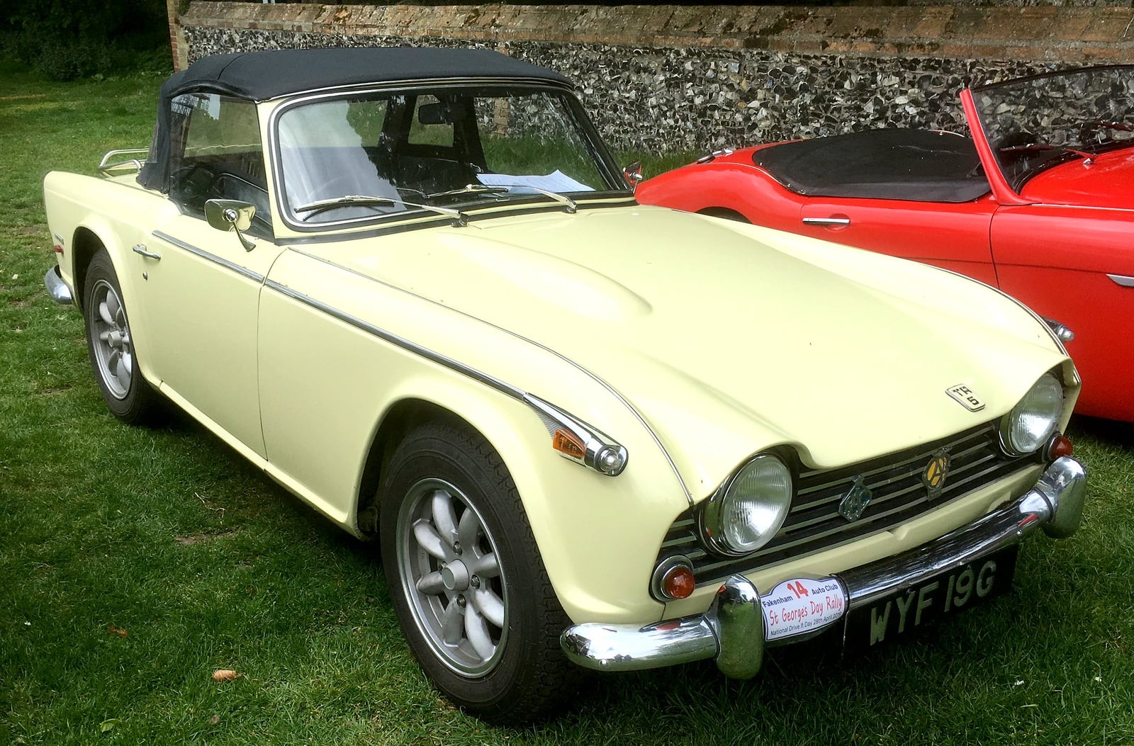 A primrose-yellow Triumph TR5 with a hardtop, front three-quarter view on a show field